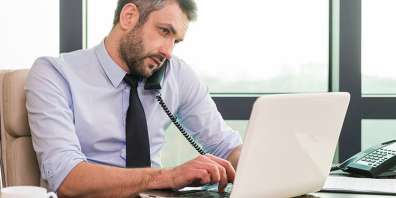 Businessman working on laptop in office while talking on phone