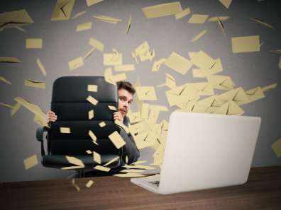 Man hiding behind chair with envelopes flying around room