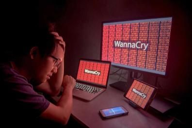 Man with hand on had and "WannaCry" displayed on three monitors