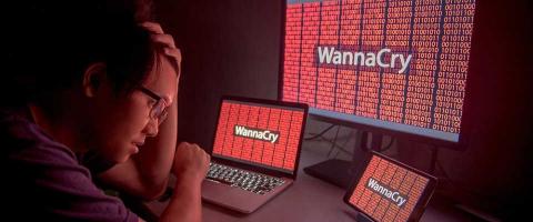 Man with hand on had and "WannaCry" displayed on three monitors