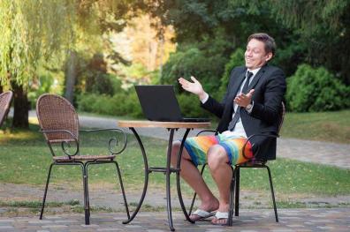 Man sitting at a patio table wearing a suit coat and tie with colored swimming trunks