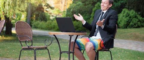 Man sitting at a patio table wearing a suit coat and tie with colored swimming trunks