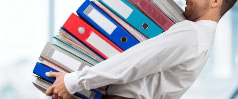 Man holding several large binders full of papers