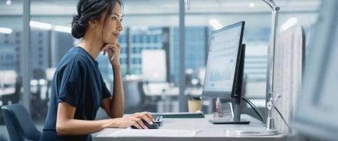 Professional businesswoman sits at an office desk starting at her computer screen signifying Managed IT Services