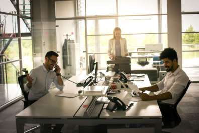 Three young professionals in a modern office setting working while one stands at an office copier signifying Managed Print Services.