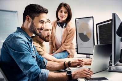 Team members gather around several computer screens with code and graphs to symbolize small business IT solutions.