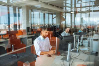 A professional setting showing a man focused on his work at a computer in a modern office with glass partitions, indicating an efficient IT solution environment.