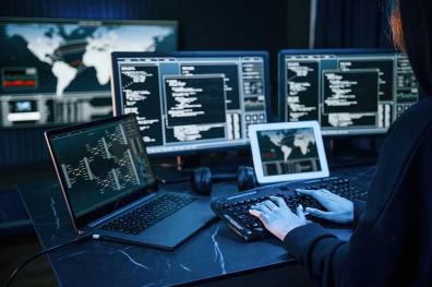 Man working behind four computer monitors with code on screen