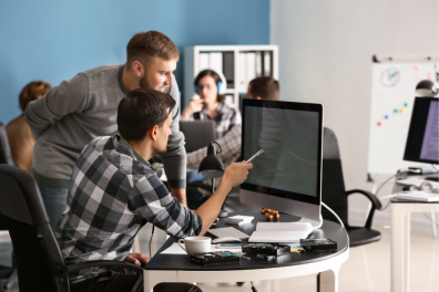 IT Services professionals collaborating in a modern office environment. Two men are focused on a computer screen, discussing code or IT solutions, representing the teamwork involved in managed IT serv