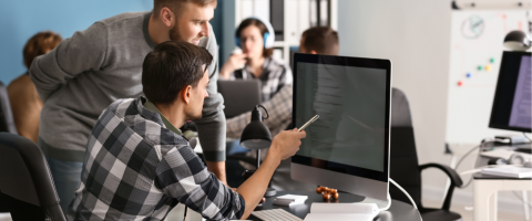 IT Services professionals collaborating in a modern office environment. Two men are focused on a computer screen, discussing code or IT solutions, representing the teamwork involved in managed IT serv