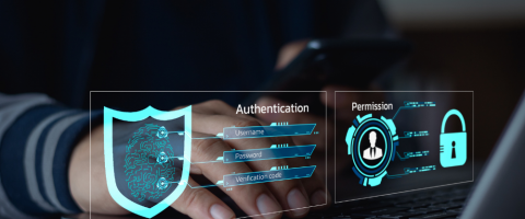 A person using a smartphone and laptop with holographic cybersecurity elements displayed, including authentication processes, permissions, and a shield icon representing digital security.