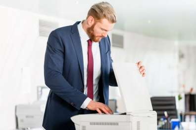 Business professional in a suit operating a multifunction printer in a modern office, showcasing the device's versatility for printing and scanning tasks.