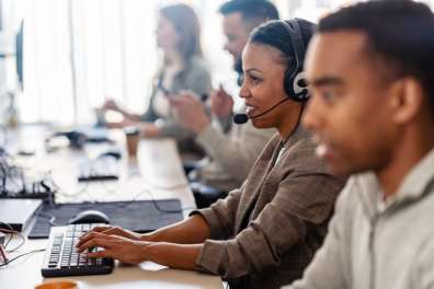 A team of professionals providing IT Support, wearing headsets and working on computers in a modern office environment.