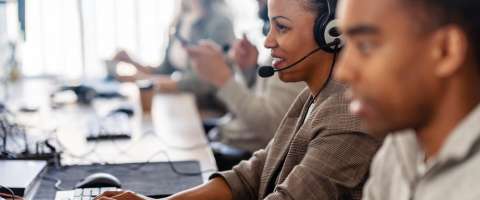 A team of professionals providing IT Support, wearing headsets and working on computers in a modern office environment.